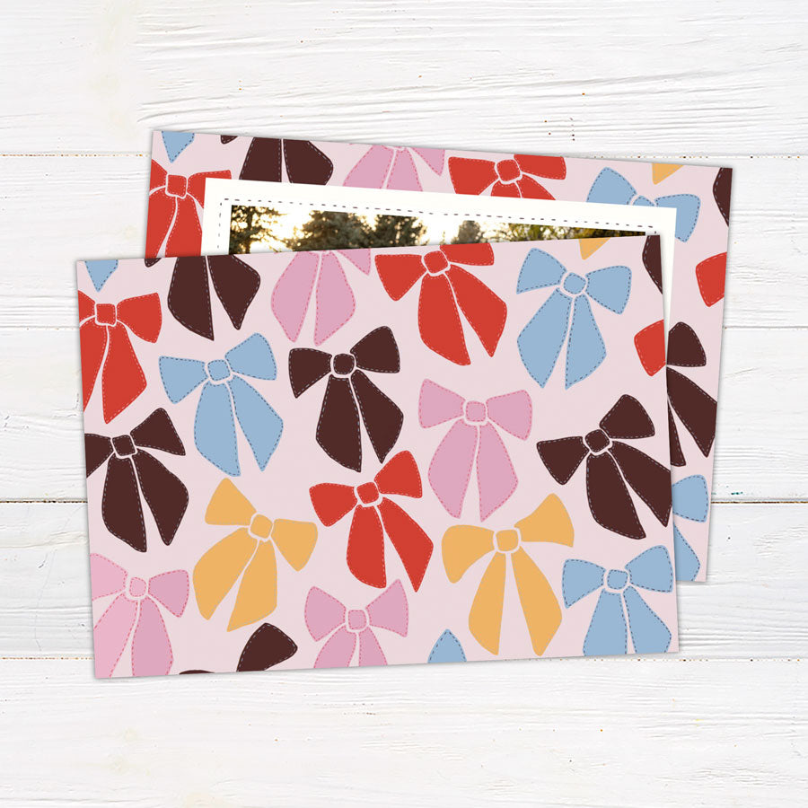 Personalized family Christmas photo card featuring a large photograph surrounded by a playful pattern of colorful ribbon bows. The coordinating back features an all-over illustrated bow pattern.
