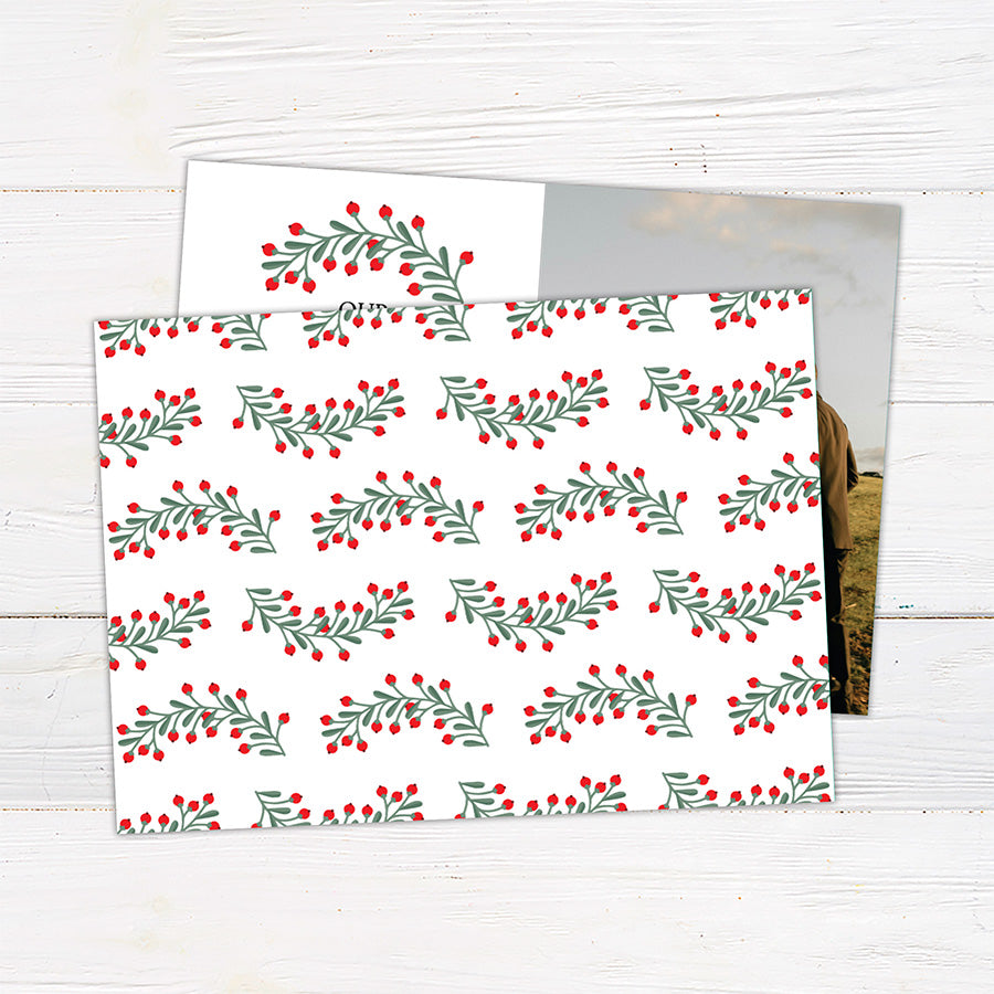 Personalized Our First Christmas photo card featuring a newlywed couple with festive greenery and red berries. The back features a coordinating botanical holiday pattern.