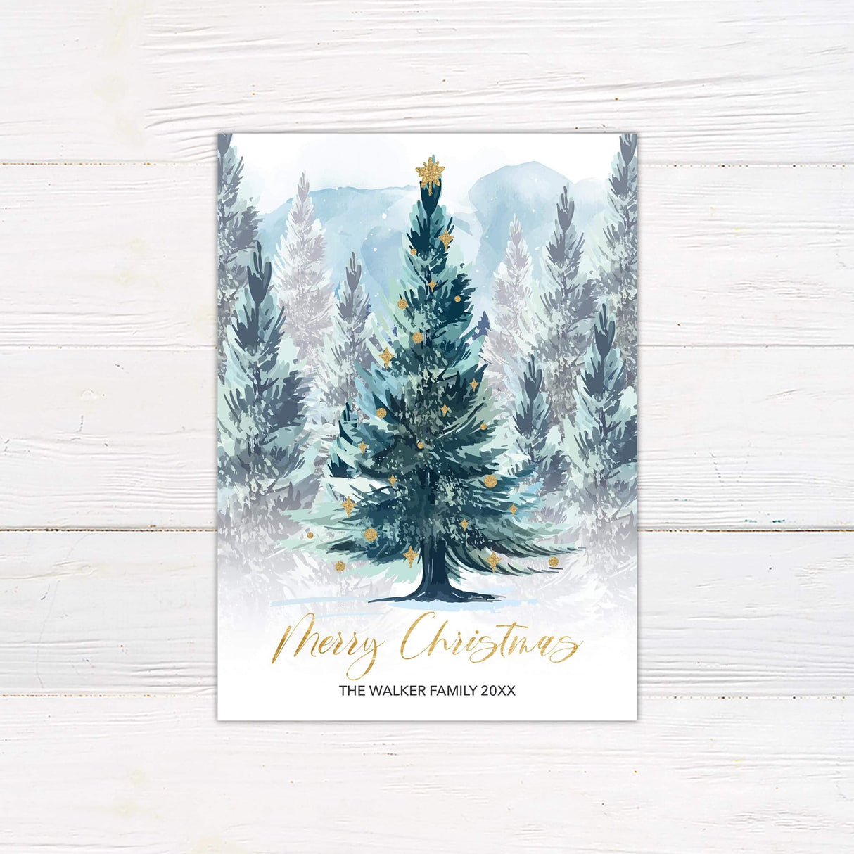 Watercolor Christmas card with decorated evergreen tree and snowy forest background, personalized with family name and year.