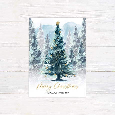 Watercolor Christmas card with decorated evergreen tree and snowy forest background, personalized with family name and year.