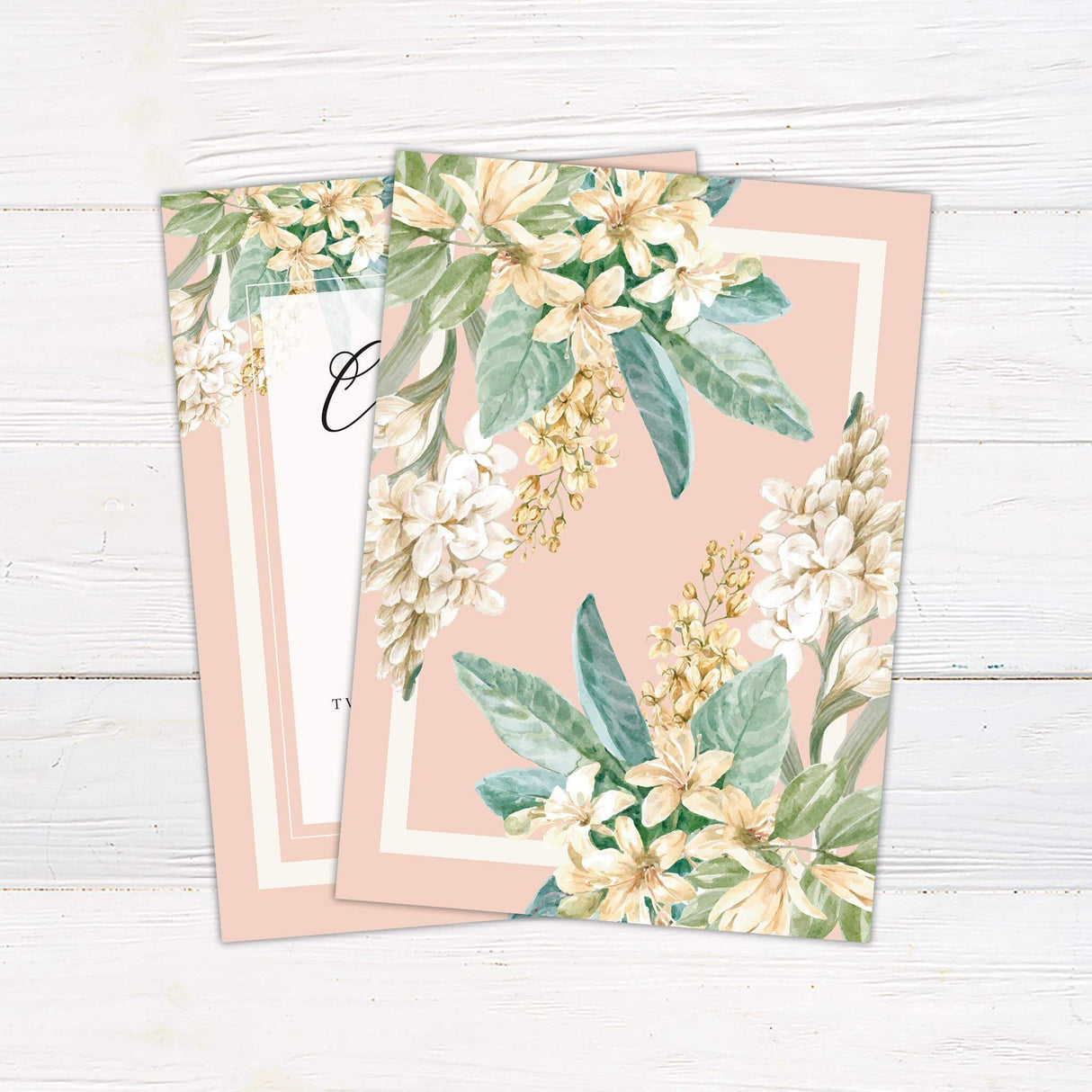 Wedding invitation with blush borders, cream center panel, white flowers, green leaves, and elegant script and serif text. - back side