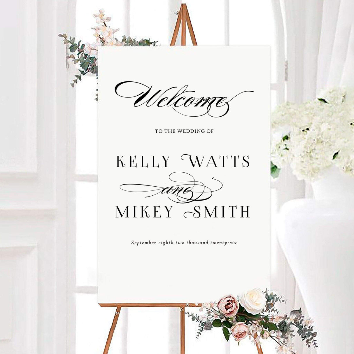 Elegant black and white paragraph style wedding welcome sign with personalized couple names in classic serif lettering and ornate calligraphy flourishes. The minimalist design includes a custom wedding date beneath the names.