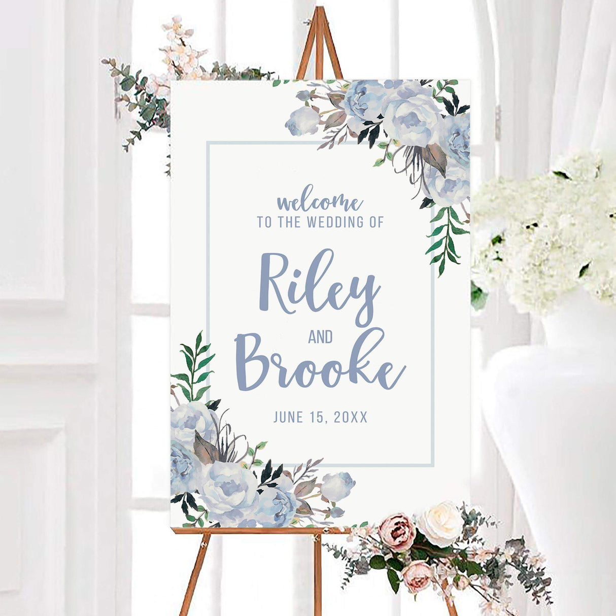 Pastel blue wedding welcome sign with watercolor flowers, greenery, and elegant personalized script. The design features the couple’s names and wedding date inside a simple rectangular border.