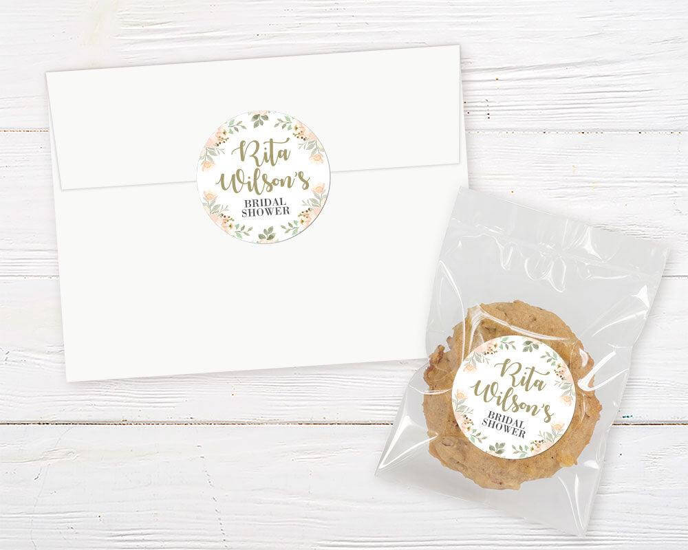 Bridal shower invitation and cookie favor with peach floral border and personalized name on rustic white wood background.
