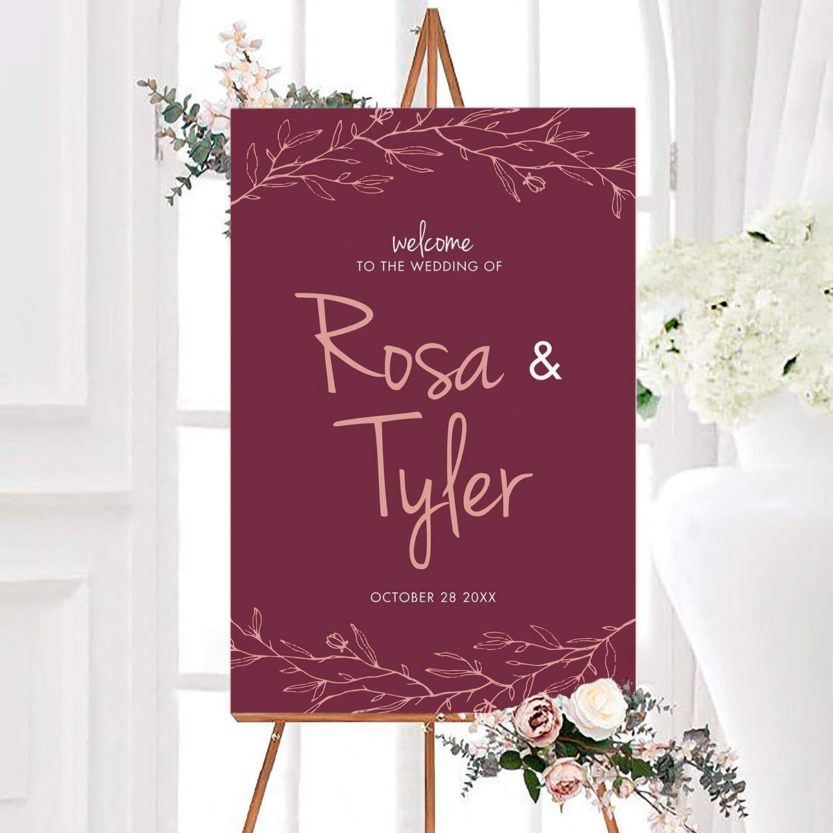 Pink branch wedding welcome sign with blush pink botanical branches framing the top and bottom. Personalized script names and the wedding date appear in the center.