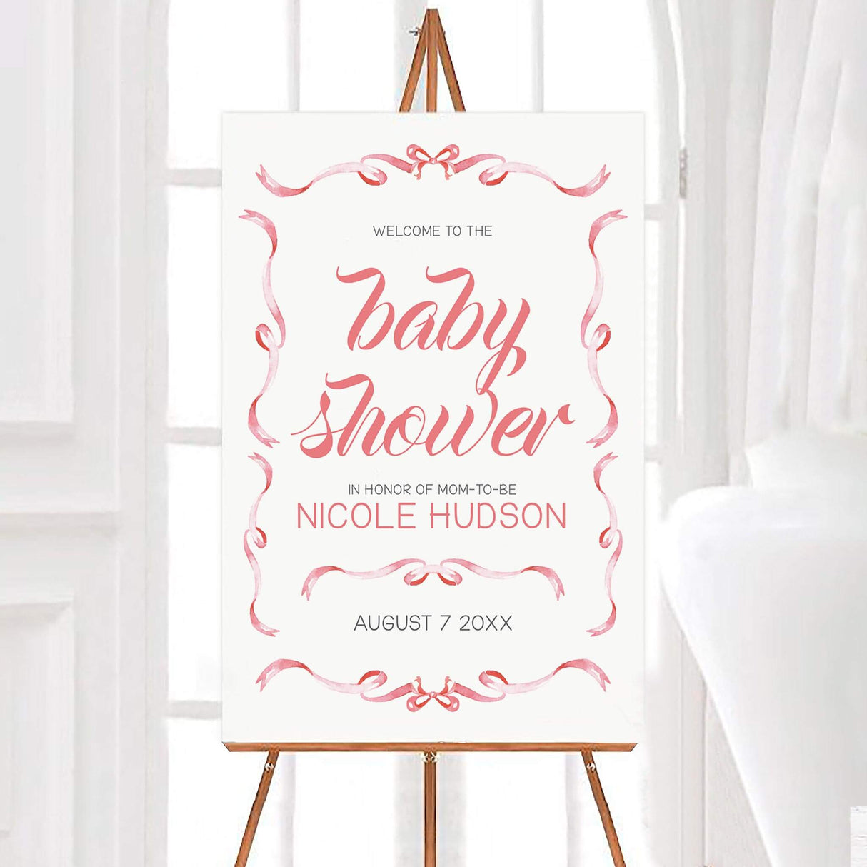 Elegant ribbons baby shower invitation with hand-lettered script and pink borders on an easel.