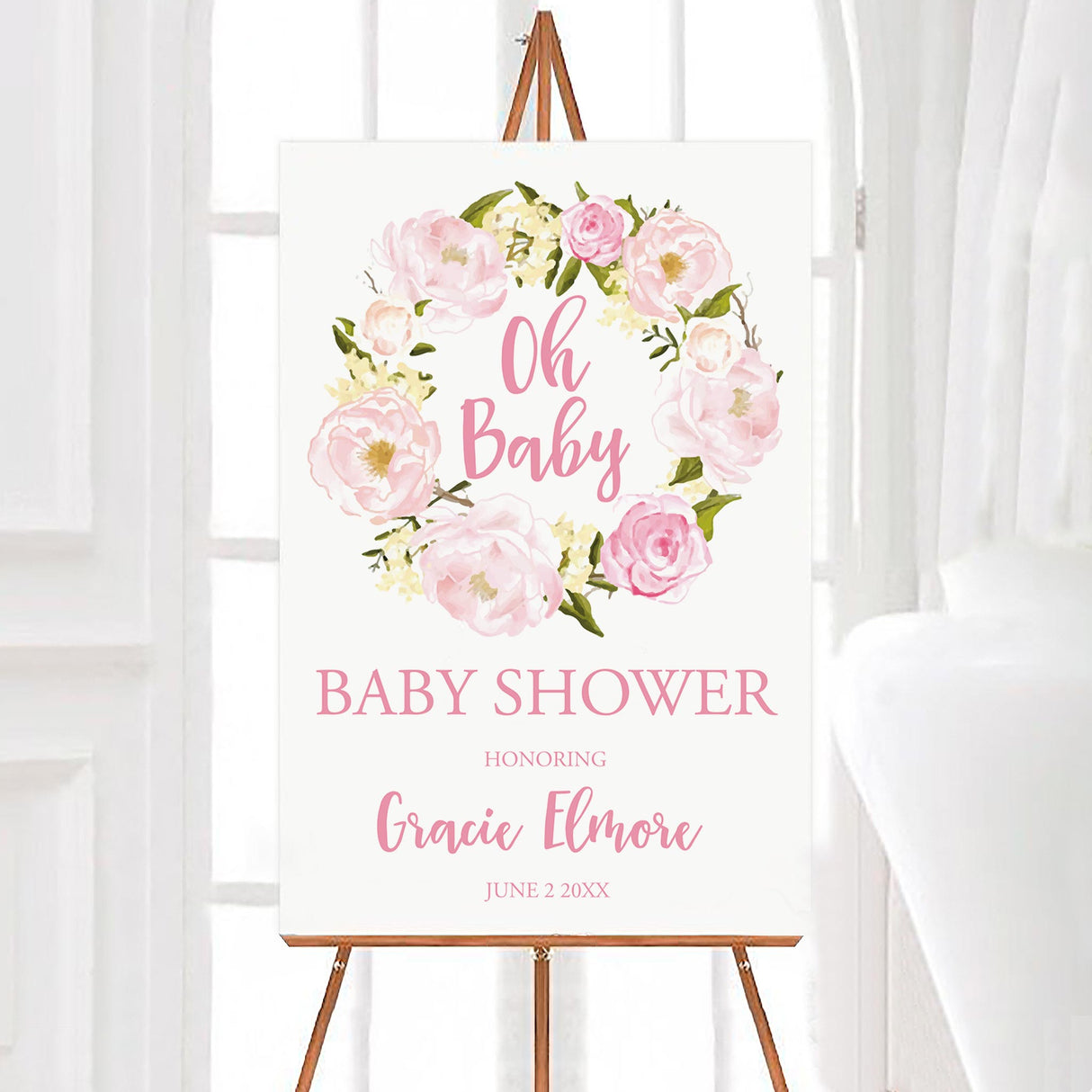A pink wreath baby shower welcome sign with a pink floral wreath and soft blush lettering. The design features flowers arranged in a circular frame on a white background.