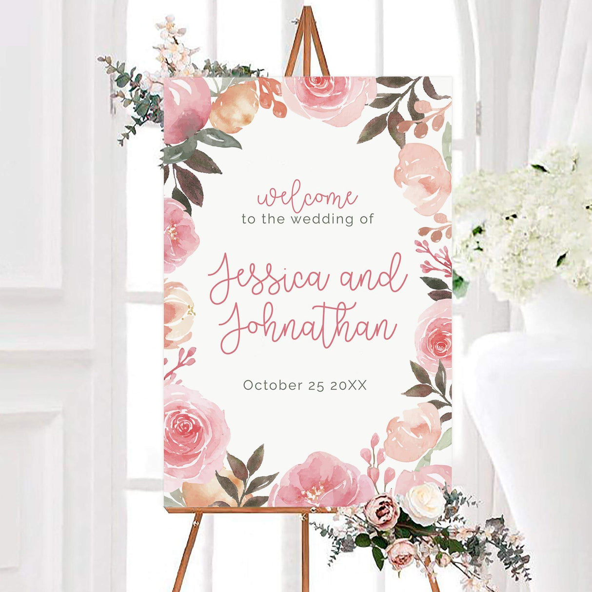Blush pink and peach wedding welcome sign with flowers and greenery framing a white center. Personalized pink script displays the couple’s names with their wedding date below.