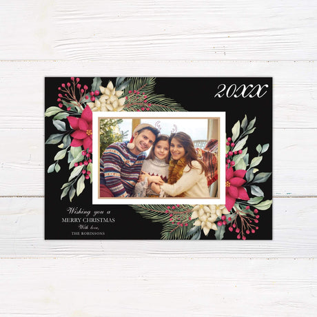 Holiday photo card featuring poinsettia floral frame on black background with personalized family photo and Christmas greeting.