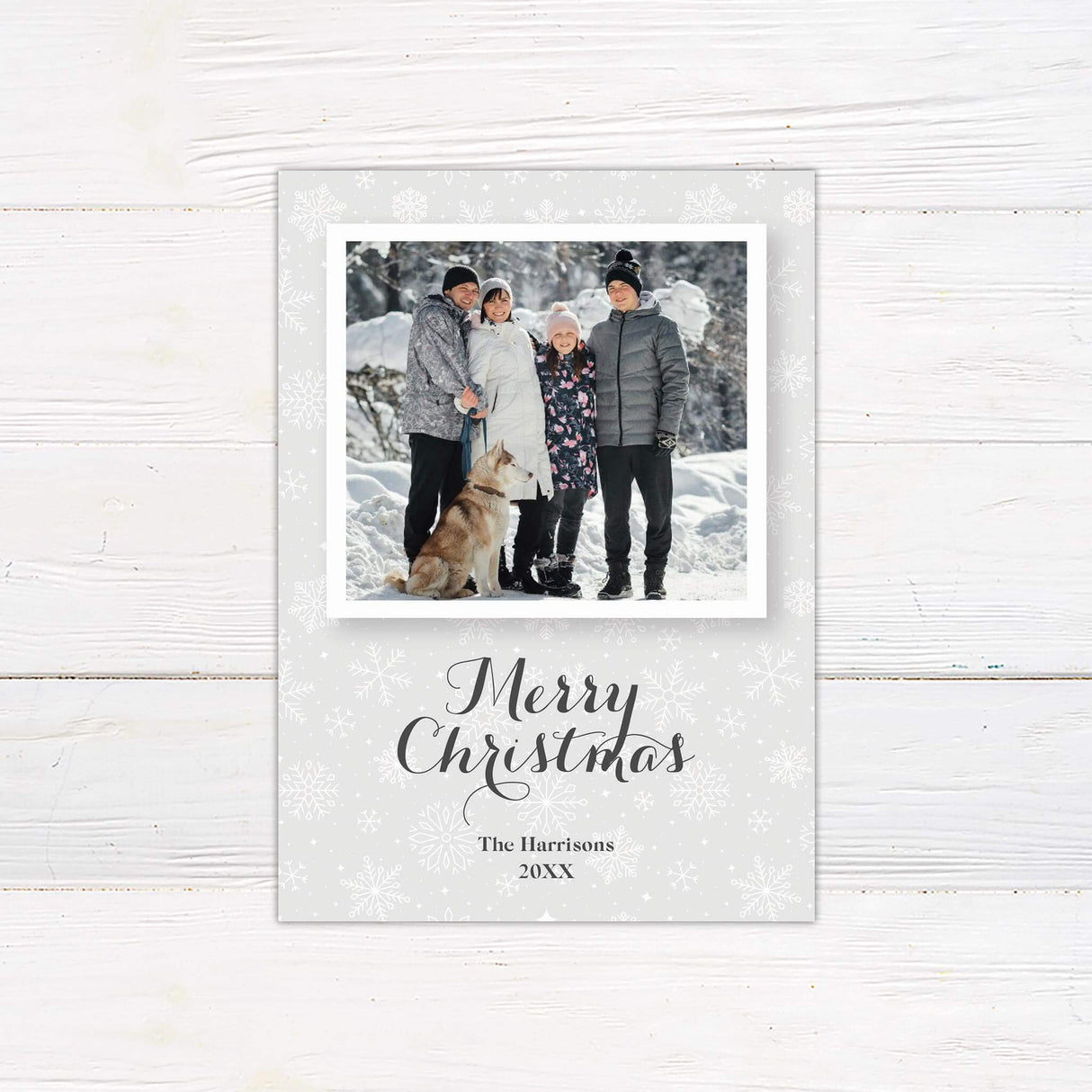 A customizable Christmas card with a central photo frame styled like a polaroid, set against a gray snowflake background for a festive holiday design.