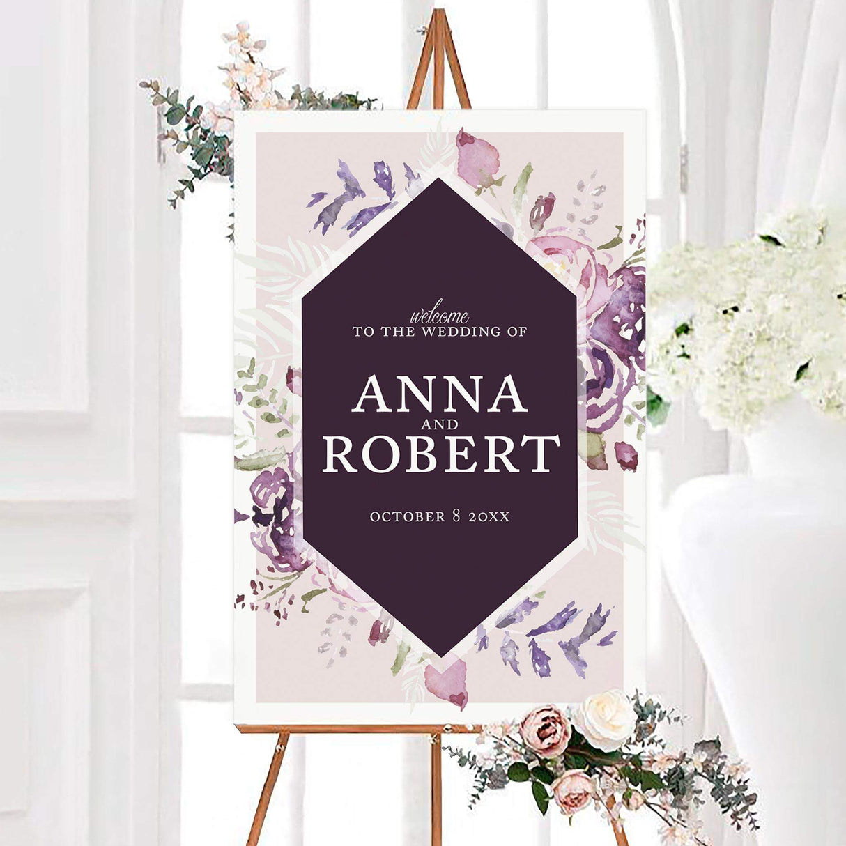 Purple blooms wedding welcome sign with a deep plum geometric center surrounded by pink, lavender, and violet watercolor flowers. White personalized lettering displays the couple’s names and wedding date.