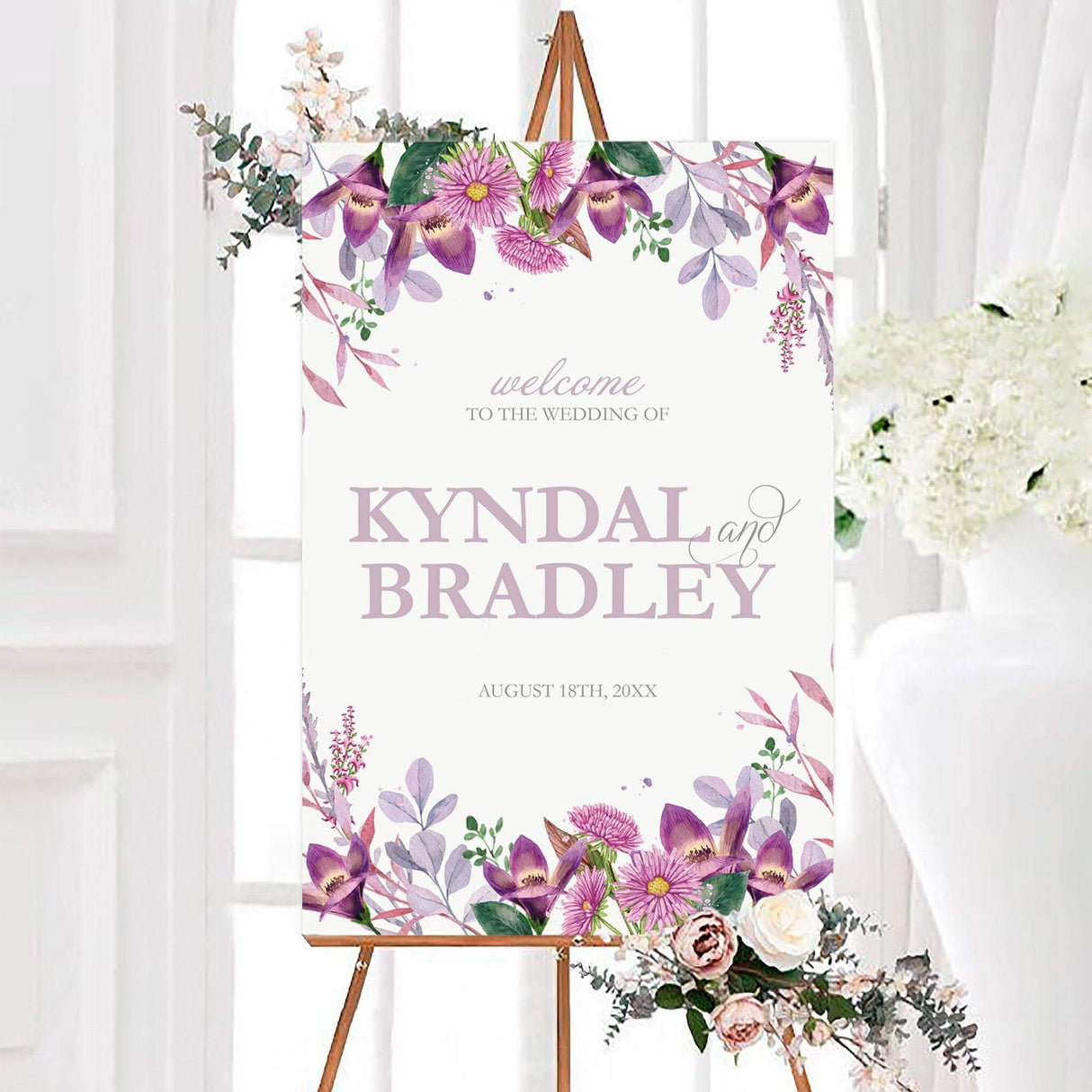 Watercolor radiant lilac wedding welcome sign framed with purple, lilac, pink, and green flowers and foliage. The personalized design features the couple’s names and wedding date on a clean white background.