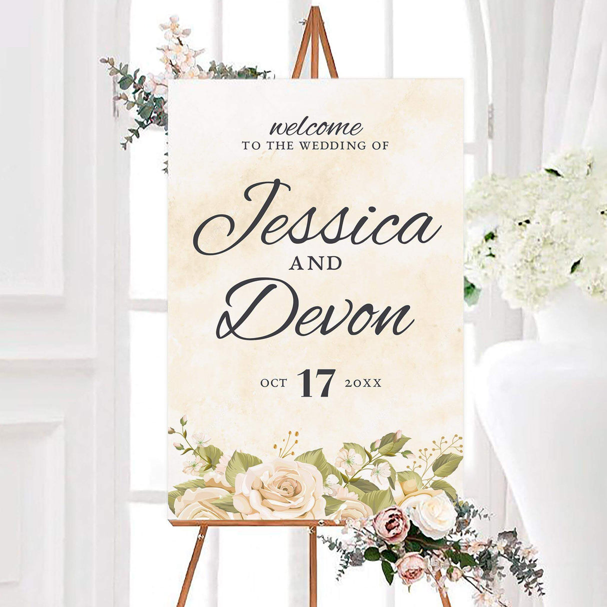 Elegant rose dream wedding welcome sign featuring large script couple names on a soft ivory watercolor background. Cream roses, white flowers, green leaves, and delicate gold botanical accents decorate the bottom.