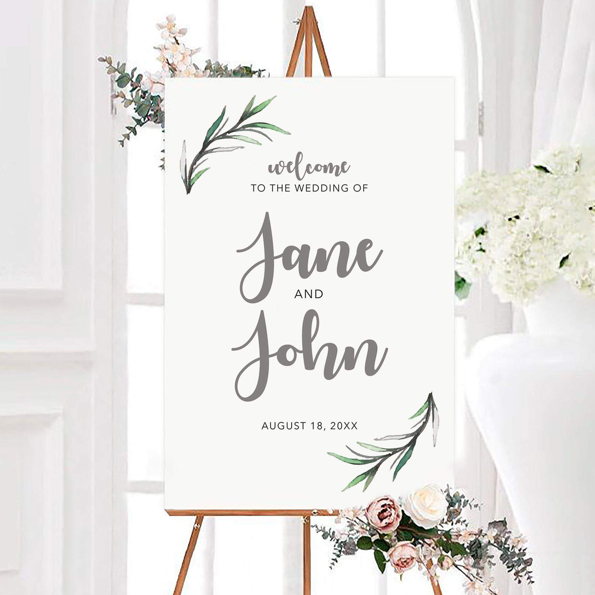 Minimal rosemary leaves wedding welcome sign with watercolor green rosemary leaves in opposite corners and personalized couple names in gray script. The white botanical sign also displays the couple’s wedding date beneath the names.