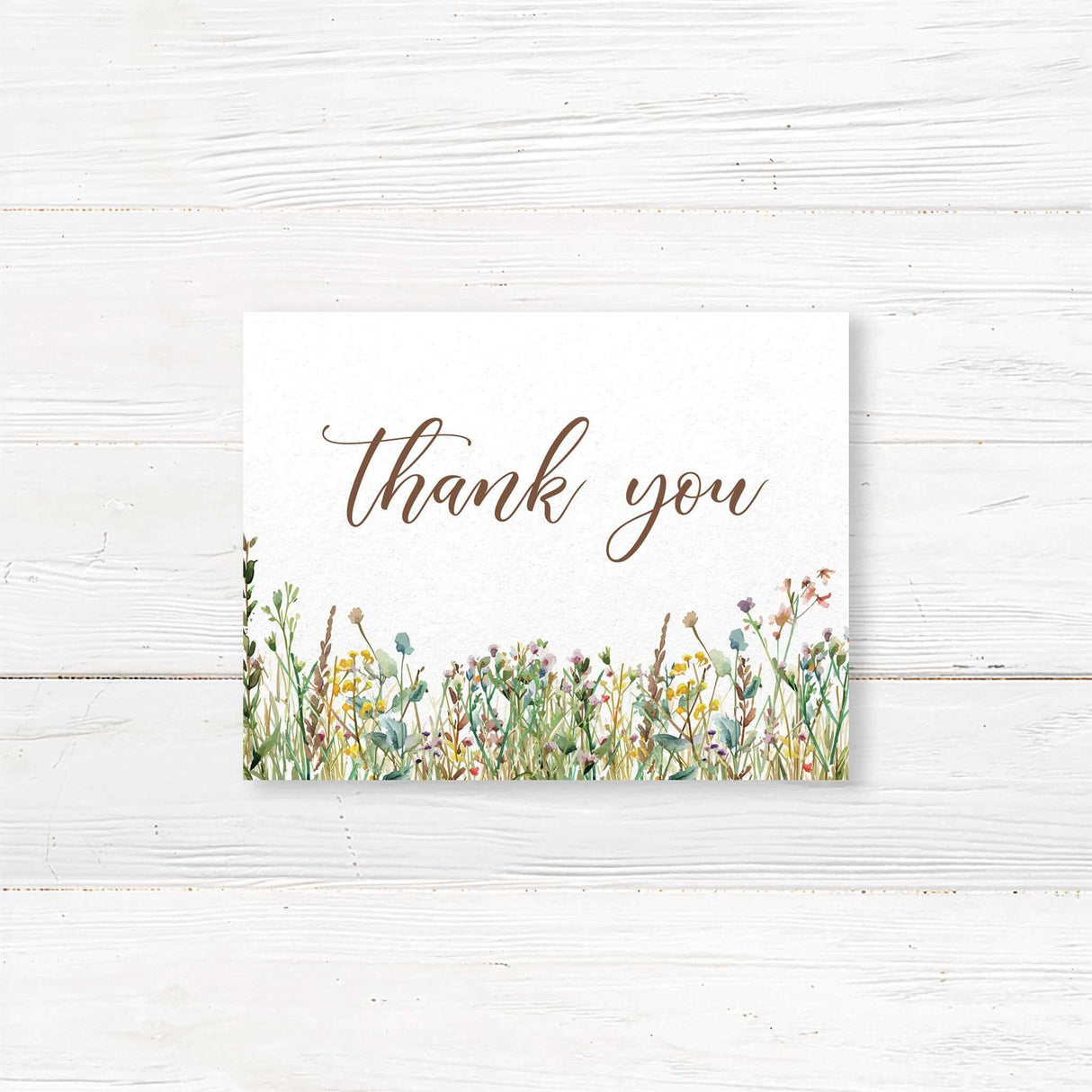 Elegant thank you card with a minimalist design featuring delicate script and serif fonts. The bottom of the card is adorned with a watercolor wildflower border, adding a rustic and romantic touch. The color palette consists of soft neutrals and earth tones, creating a timeless and sophisticated look.