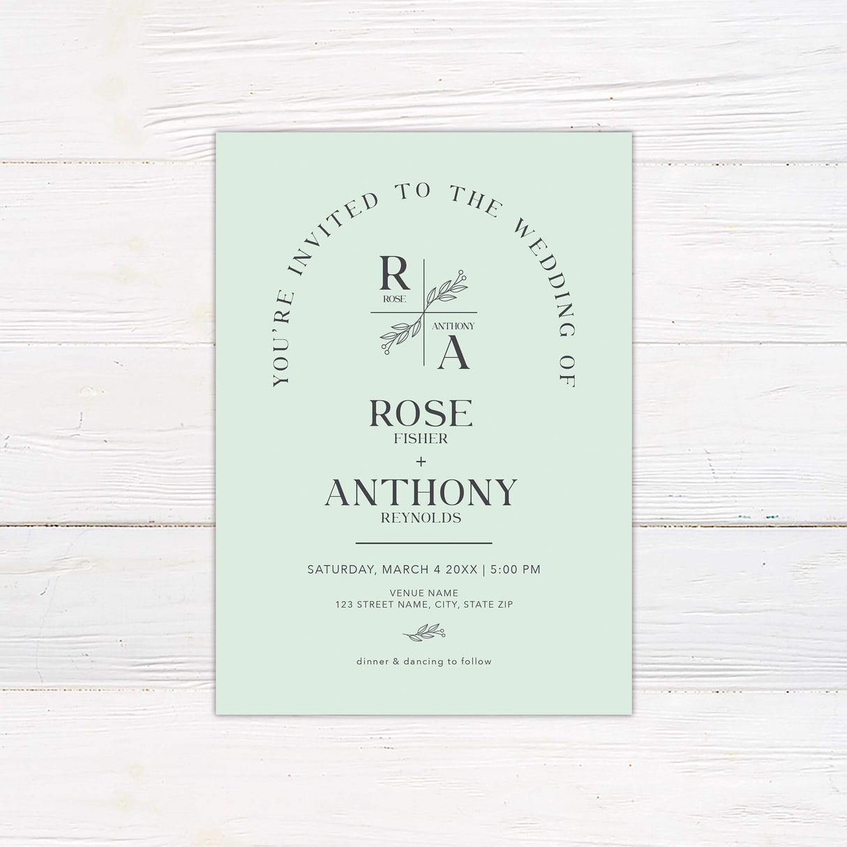 Minimalist monogram wedding invitation with botanical crest and arch layout in modern green tones