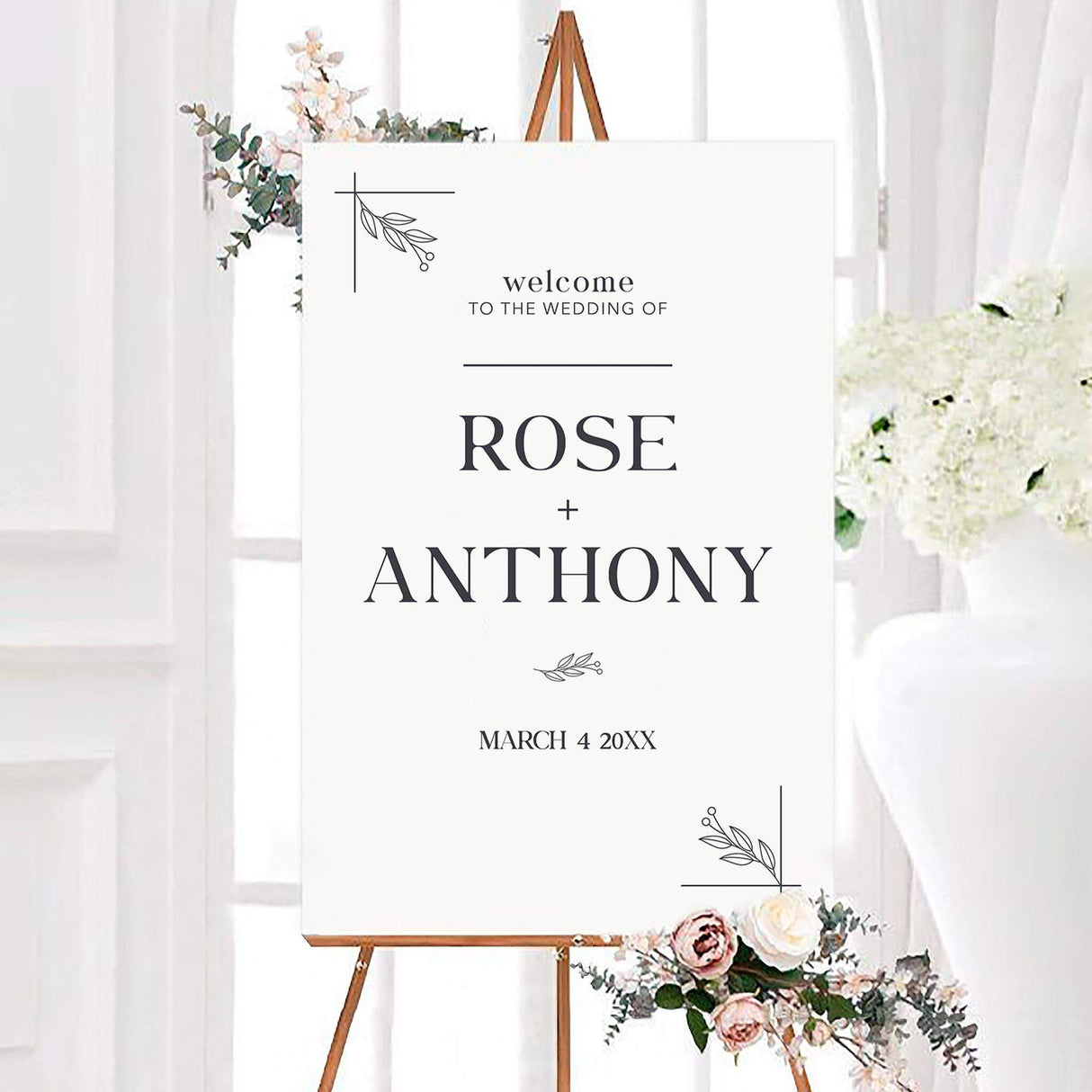Simple arch wedding welcome sign with charcoal serif lettering, personalized couple names, and delicate botanical line art. Simple leafy corner accents and a wedding date complete the clean black and white design.