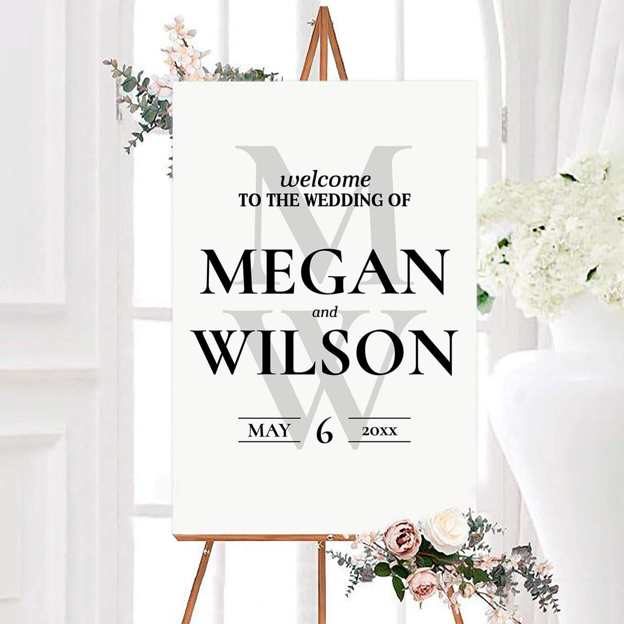 Simple bold minimalist wedding welcome sign featuring bold serif names over oversized light gray monogram initials. The personalized design includes the couple’s names and wedding date on a clean white background.