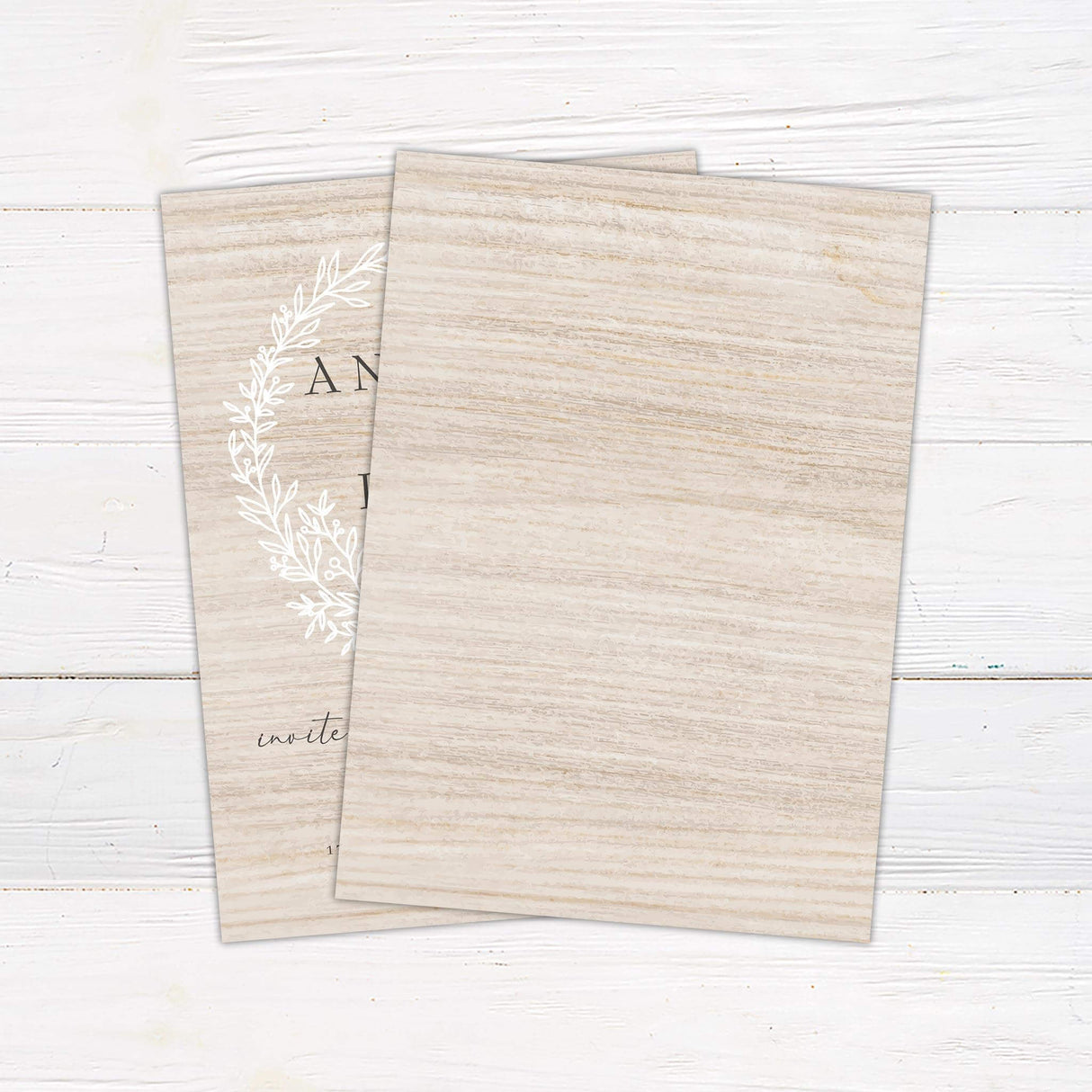 Rustic wedding invitation with white wreath design on woodgrain background and minimalist serif and script fonts- back side