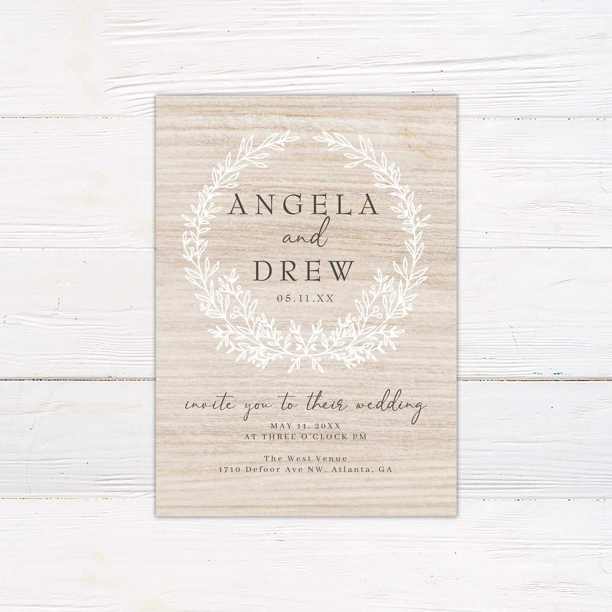 Rustic wedding invitation with white wreath design on woodgrain background and minimalist serif and script fonts