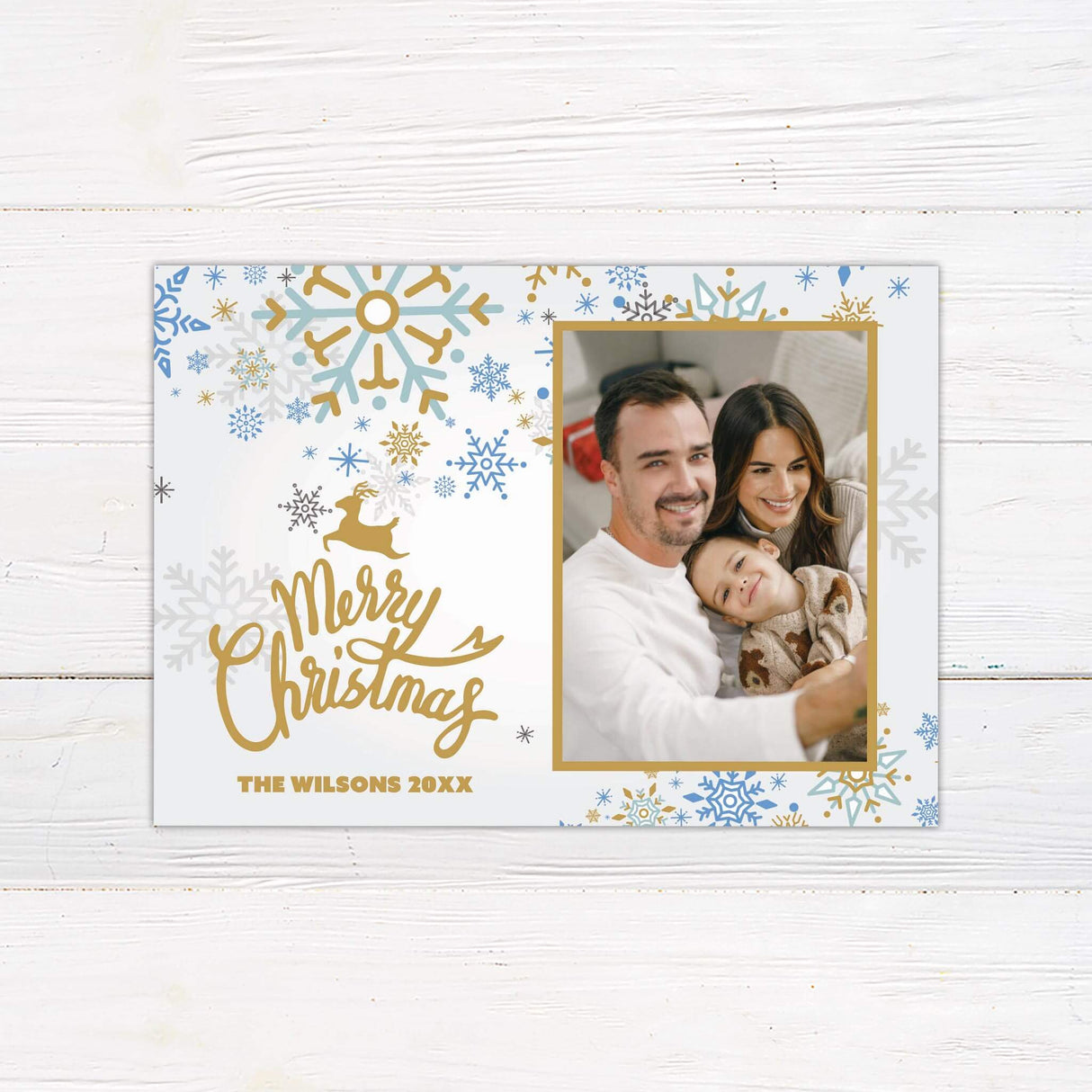 A holiday card with gold and blue snowflakes featuring a family photo. The design includes “Merry Christmas” text and customizable family name.