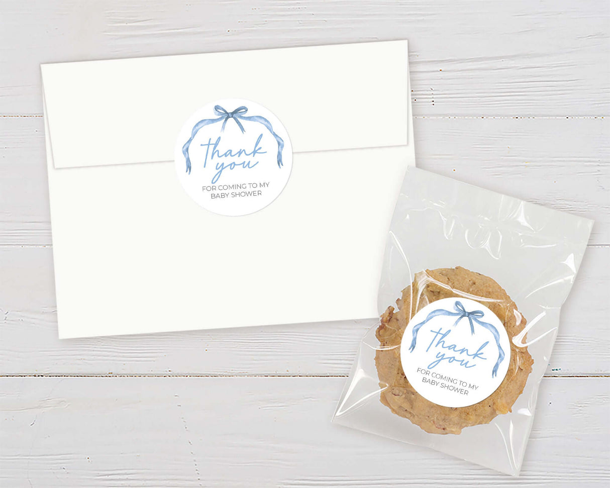 White envelope and cookie with blue ribbon 'thank you' stickers for baby shower favors.