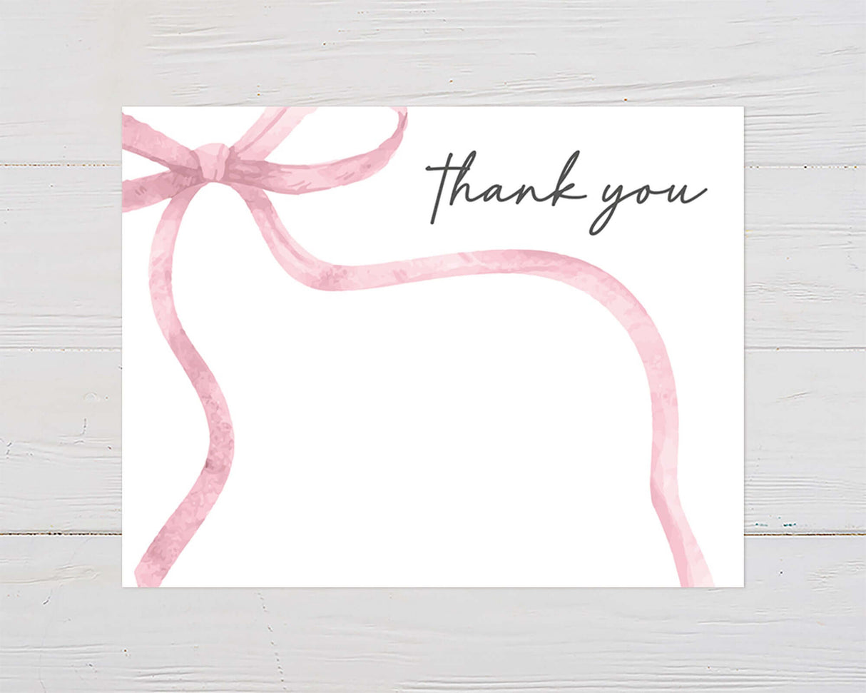 Pink ribbon thank you card on white wood background with elegant typography, ideal for baby shower invitations or gratitude notes.
