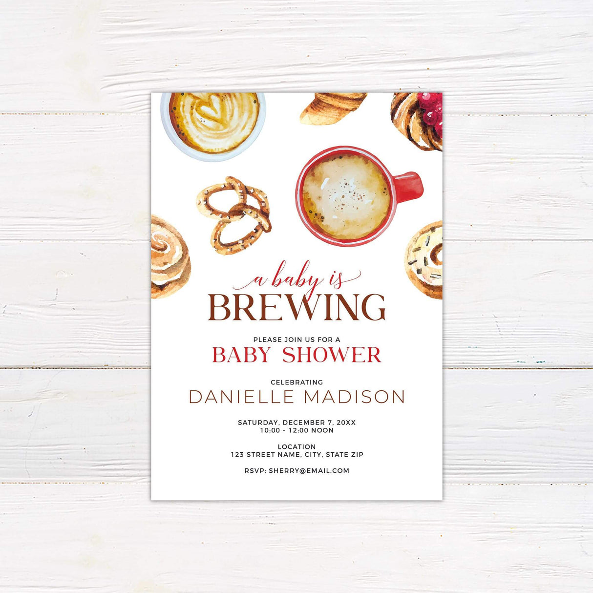 Baby shower invitation with a cozy coffee and pastry theme. Features watercolor illustrations of a red coffee cup, latte art, croissants, cinnamon rolls, pretzels, and cookies on a light background. The phrase "A Baby is Brewing" is written in elegant script, with event details such as date, time, location, and RSVP information displayed in a mix of serif and script fonts. The warm tones and inviting design create a charming and stylish invitation, perfect for a coffee-inspired baby shower.