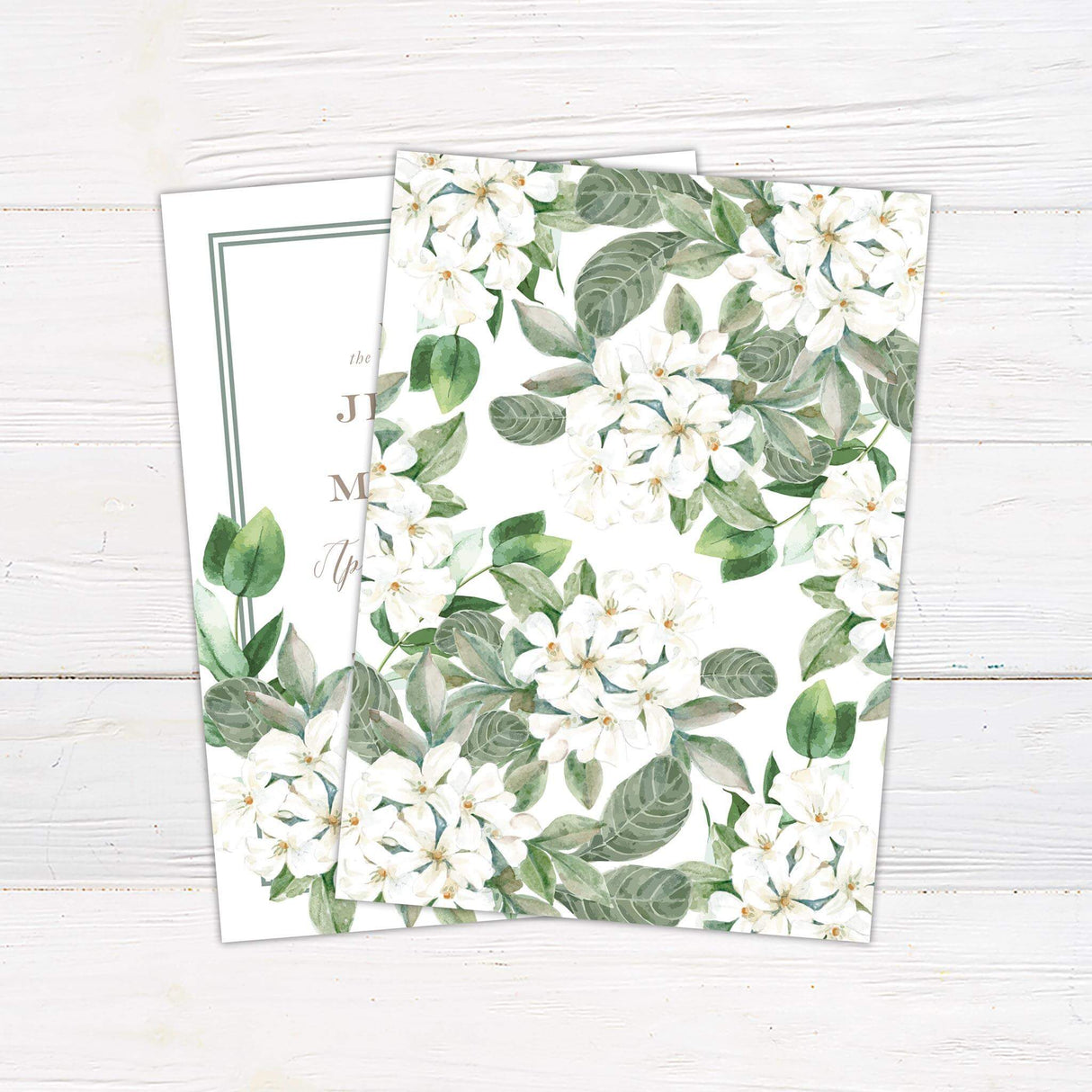 Elegant wedding invitation with watercolor white florals, green foliage, and classic serif and script fonts on a cream background with a double border frame.- back side
