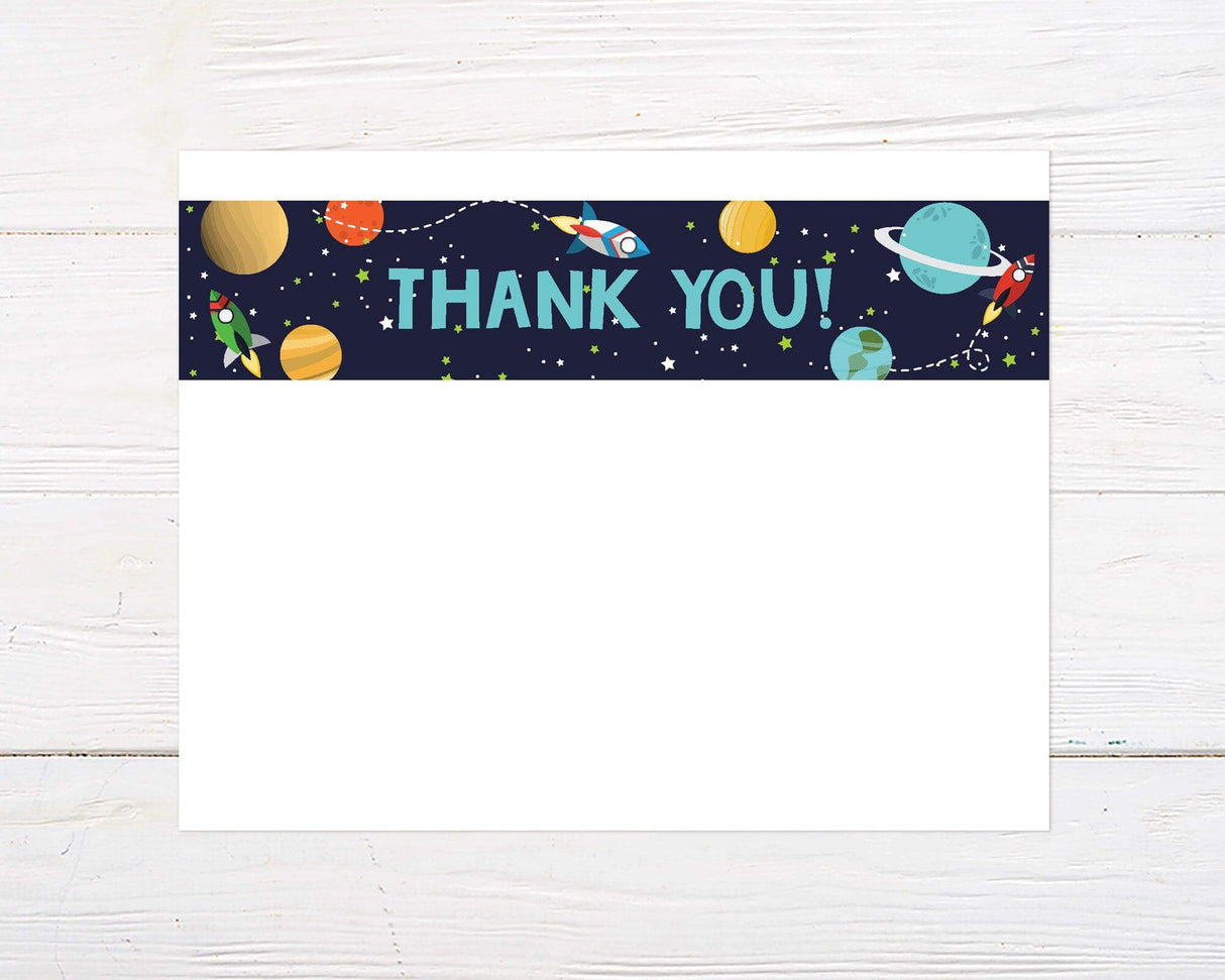 This thank you card features colorful planets, stars, and rocket ships scattered across a dark space-themed background. The words "Thank You!" are boldly written in large green letters at the center of the top space border.