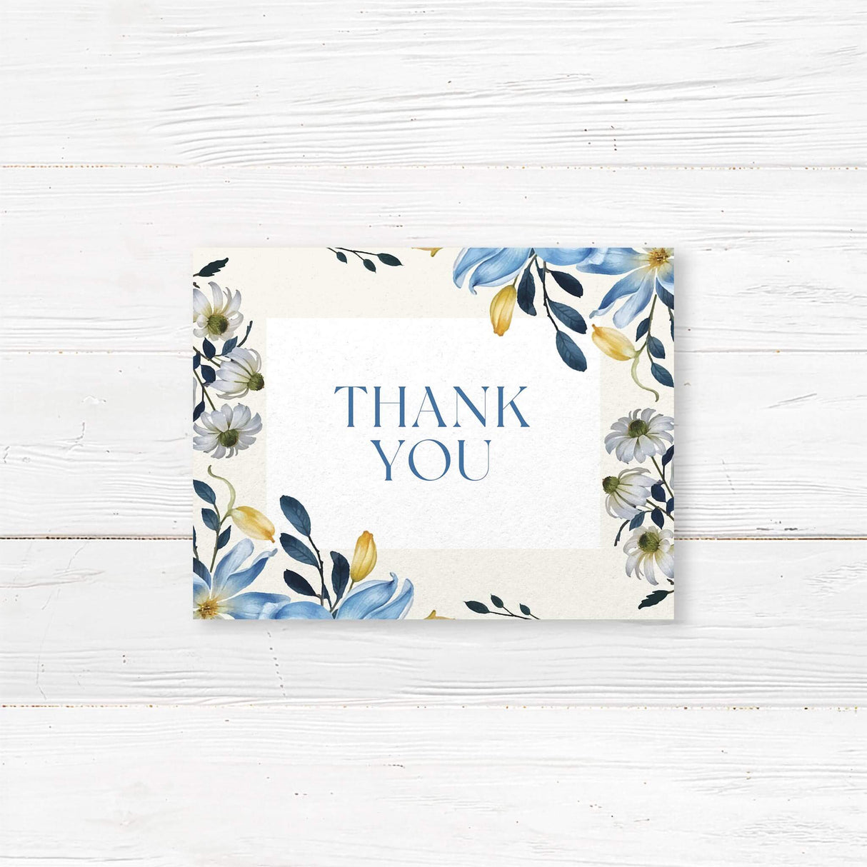A thank you note card with a soft cream background features an elegant floral border of blue, white, and yellow flowers with lush greenery. The text is centered within a white rectangle, using a mix of serif and script fonts for a sophisticated and timeless look. Event details, including the date, time, and venue, are clearly displayed. The design combines classic elegance with a modern floral touch.