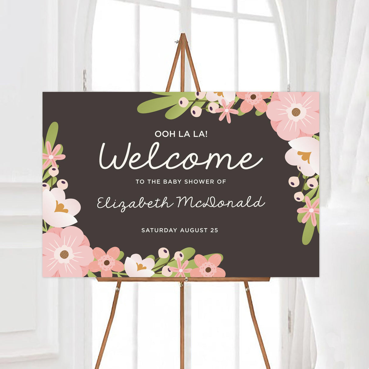 A spring floral baby shower welcome sign with pink flowers and green leaves on a dark background. The design has a soft floral border and elegant text.