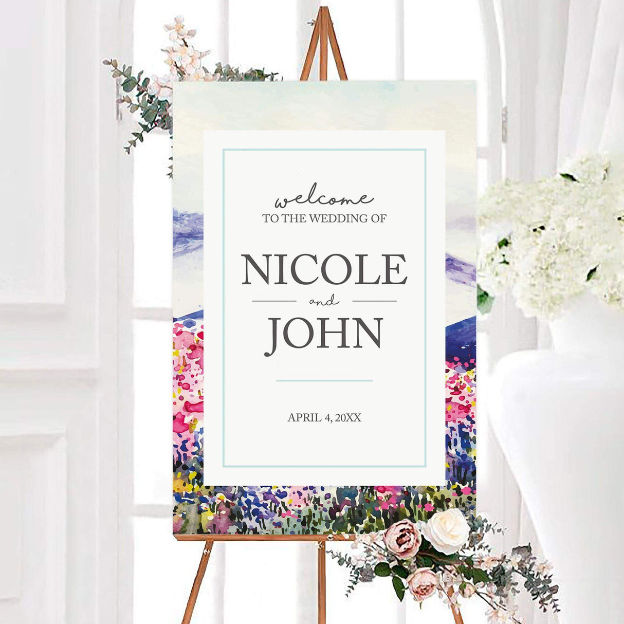 Colorful watercolor spring landscape wedding welcome sign with flowers, rolling hills, and a white personalized center panel. The design features the couple’s names and wedding date in elegant gray lettering.