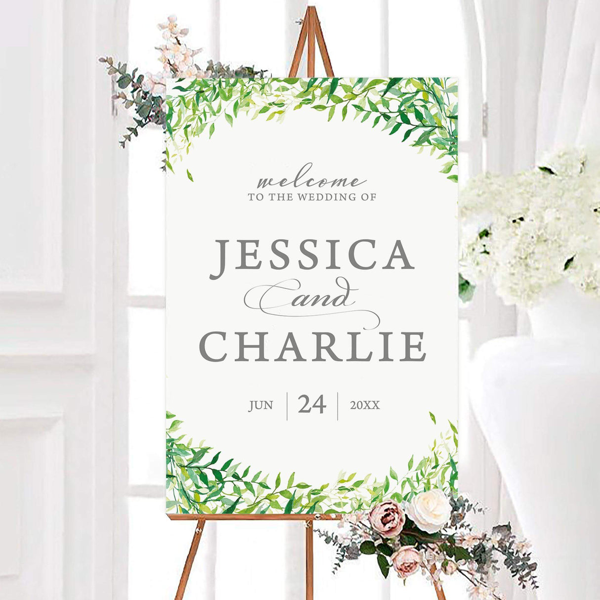 Watercolor sprinkled leaves wedding welcome sign with a leafy green botanical border and elegant gray lettering. The personalized design features the couple’s names and wedding date on a white background.