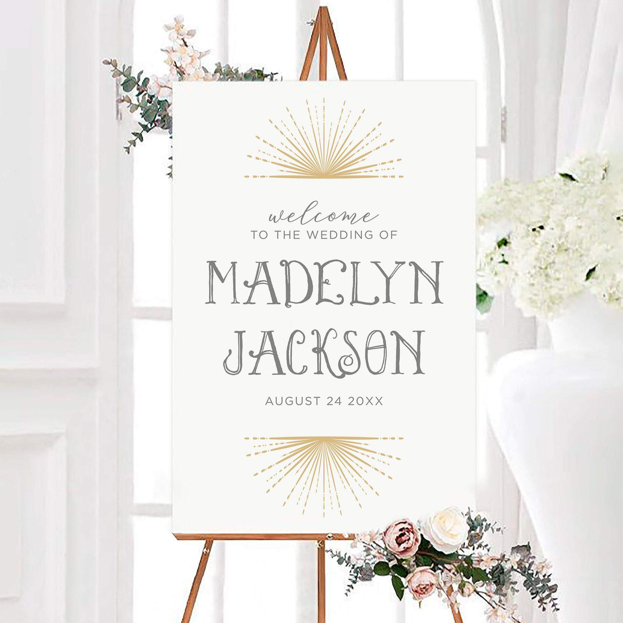 Elegant starburst wedding welcome sign with golden starburst rays, gray lettering, and personalized couple names. The modern celestial design includes the couple’s wedding date beneath the names.