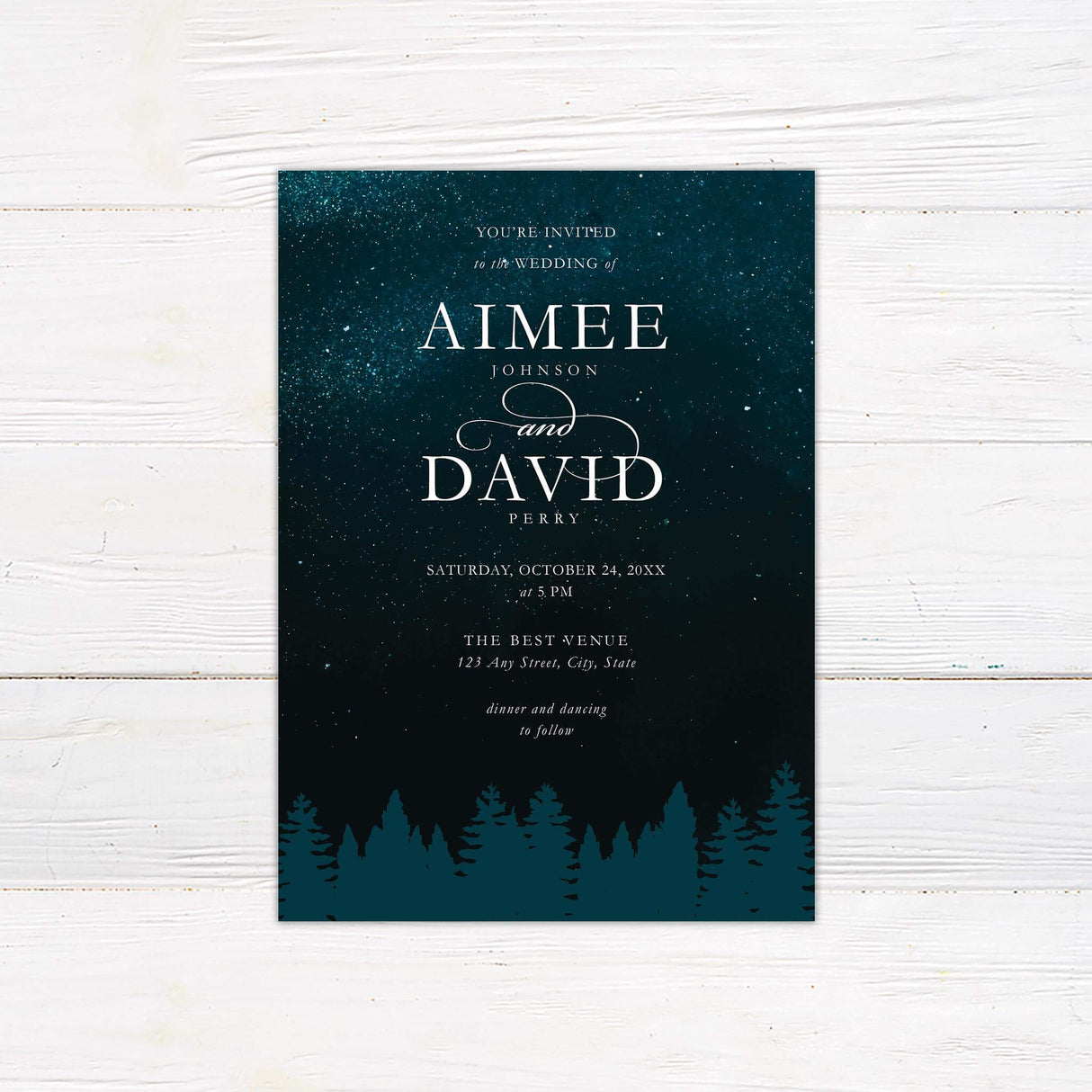 Wedding invitation with dark teal starry sky, silhouetted pine forest treeline, and elegant serif and script fonts for a romantic celestial wedding.