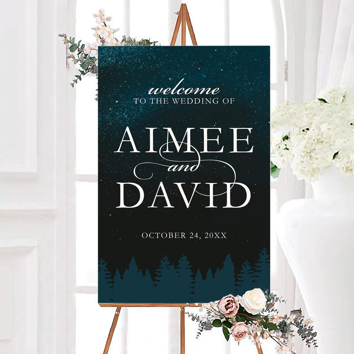 Starry treeline wedding welcome sign with white typography on a dark teal sky and evergreen forest silhouette. The personalized design features the couple’s names and wedding date.