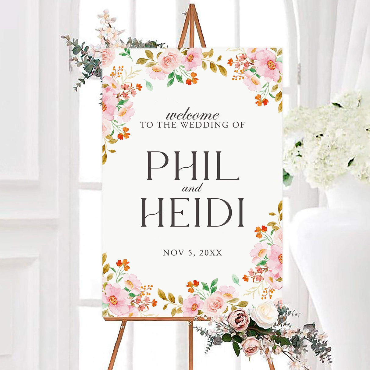 Sweeping floral vine wedding welcome sign featuring watercolor pink roses, blush flowers, orange accents, and green and golden foliage. The white-centered floral design displays the couple’s names and wedding date in elegant typography.