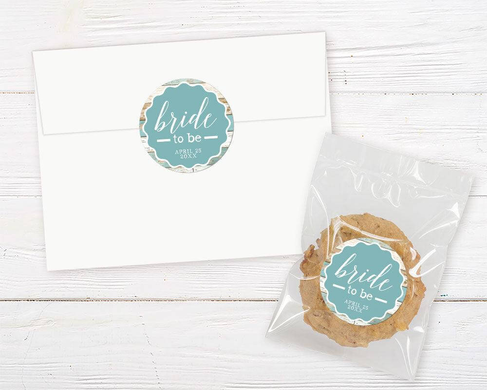 A teal wood bridal shower invitation sticker with white text and a rustic wood background. The design features a clean layout with a modern script font.