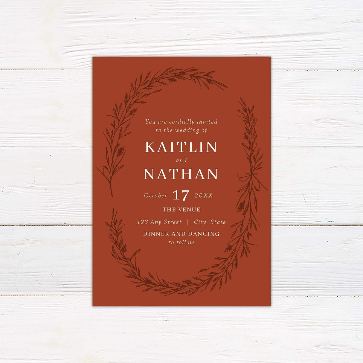 Burnt orange wedding invitation featuring a hand-drawn foliage wreath and white serif text, perfect for fall and rustic-themed weddings.