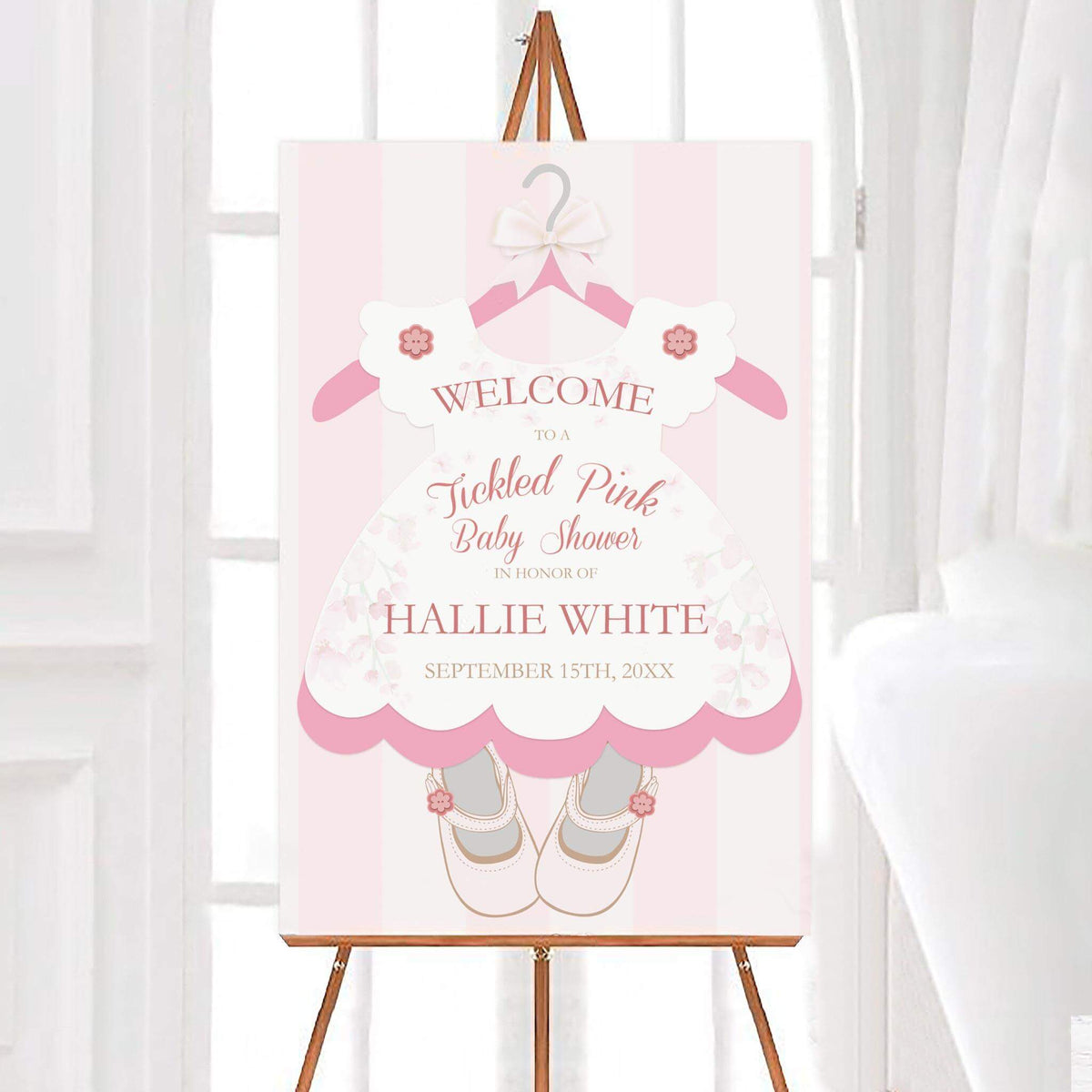 Personalized Tickled Pink baby shower welcome sign featuring a pink floral baby dress, white bow, decorative hanger, and matching baby shoes. The design includes soft pink stripes, elegant lettering, and customizable name and event date.