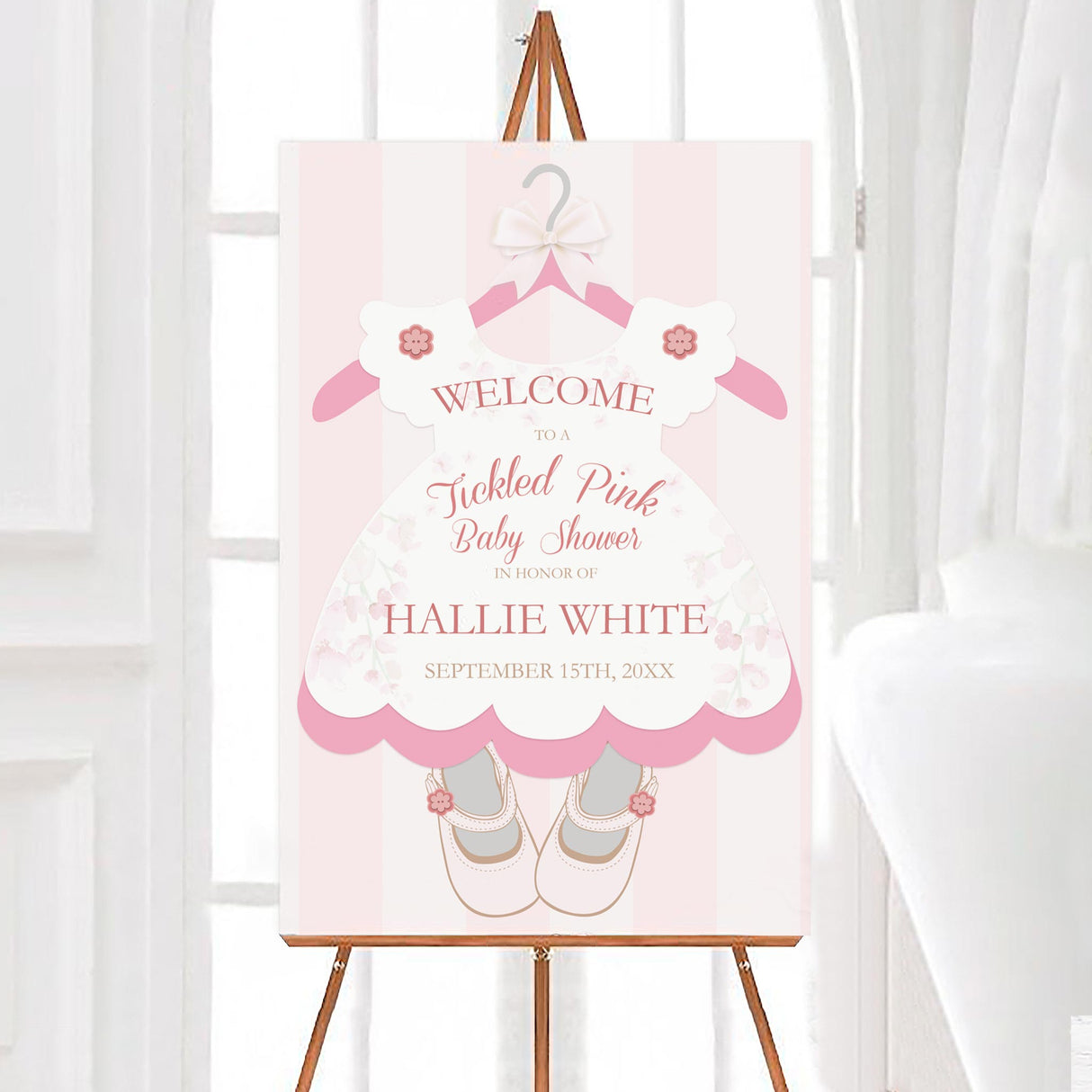 A tickled pink baby shower welcome sign shaped like a dress with ballet shoes. The design features soft floral accents and light pink stripes.
