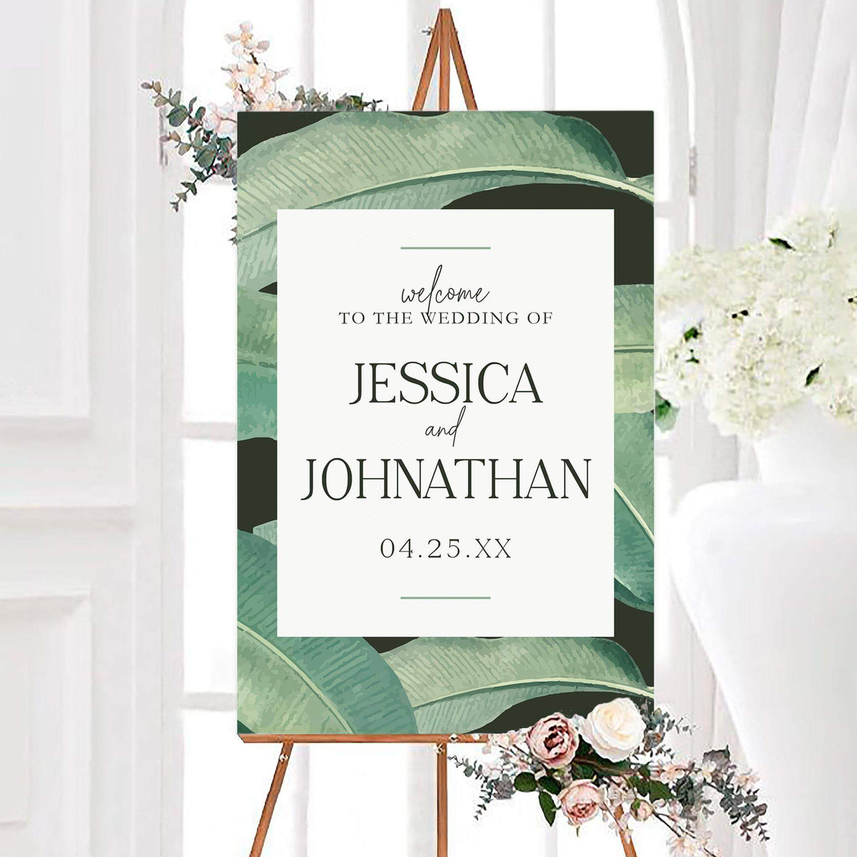 Personalized tropical leaves wedding welcome sign surrounded by large tropical green leaves with elegant couple names and a wedding date. The clean white center features classic serif lettering with delicate script accents.