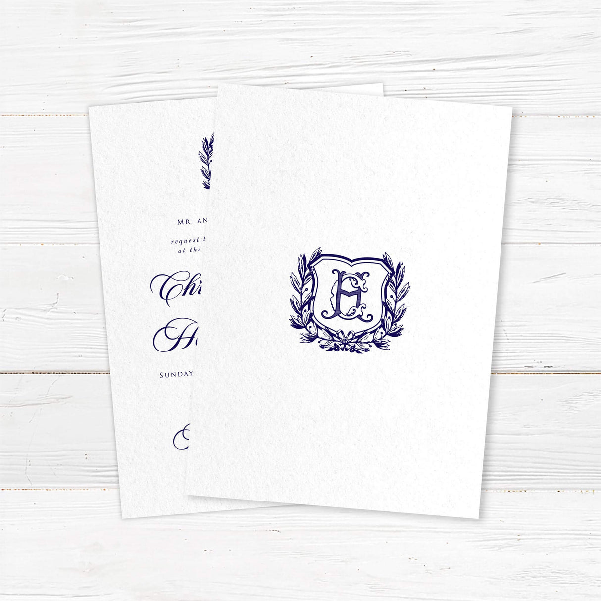 Formal wedding invitation with a vintage-style shield and laurel wreath monogram. Features elegant script for the names and classic serif text for wedding details.- back
