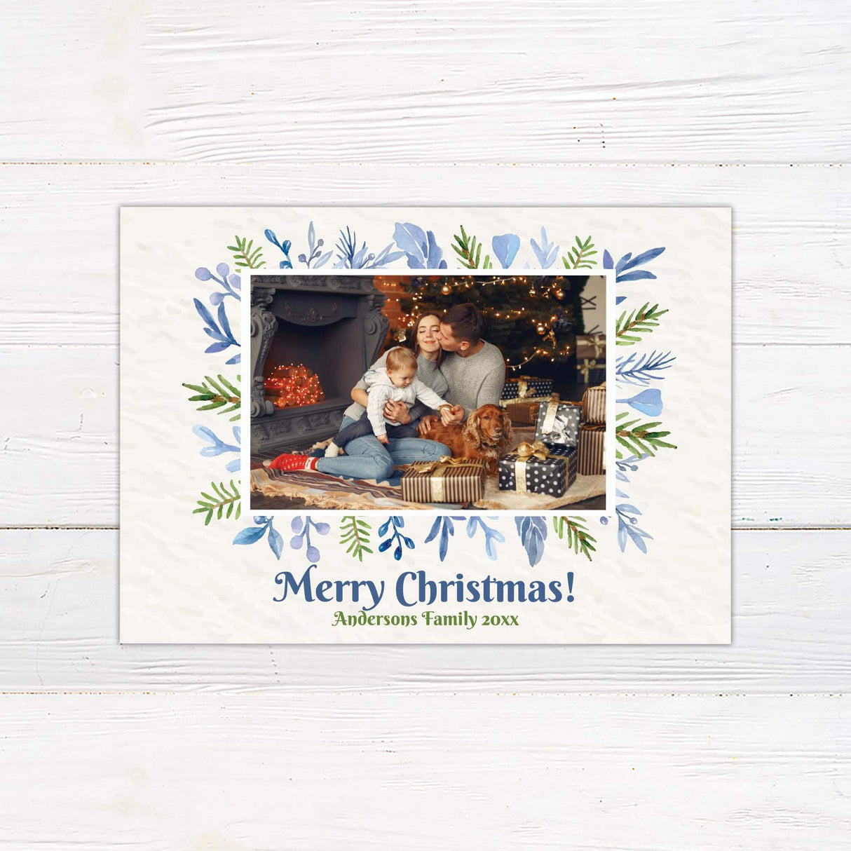 A holiday card with a family photo framed by watercolor greenery and leaves. The card includes a Merry Christmas message with customizable family name.