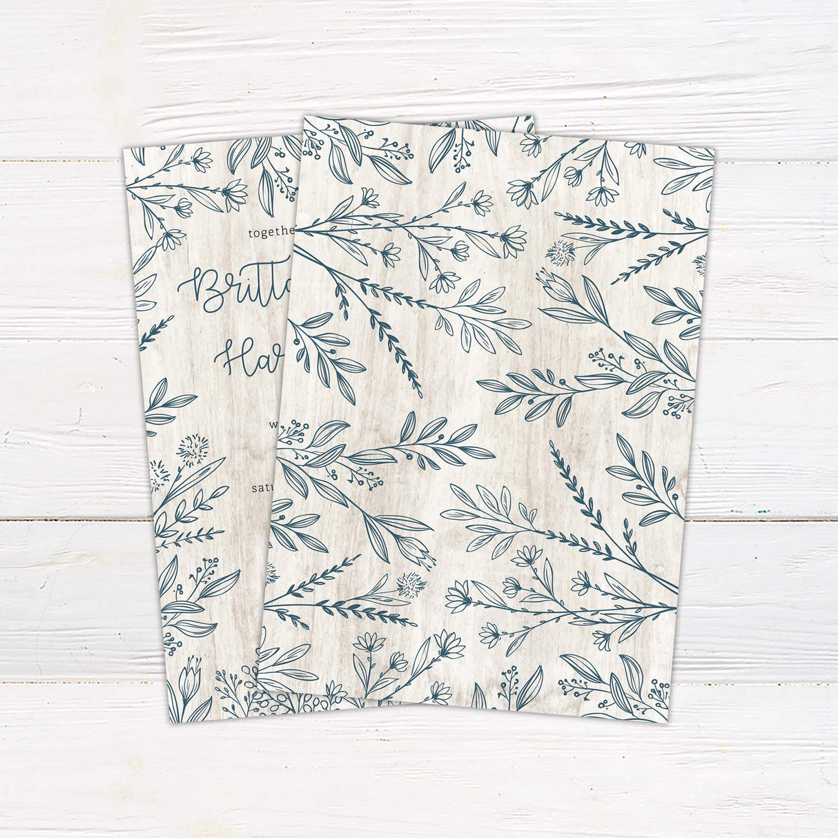Rustic wedding invitation with hand-drawn blue-gray botanical border on a white wood background and script and serif fonts.- back side