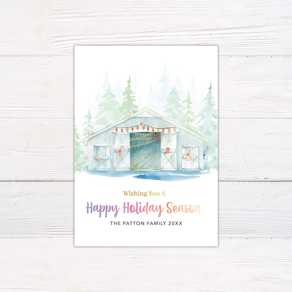 Watercolor holiday card featuring a snowy barn with festive string lights, evergreen trees in the background, and "Wishing You a Happy Holiday Season" in gradient text.