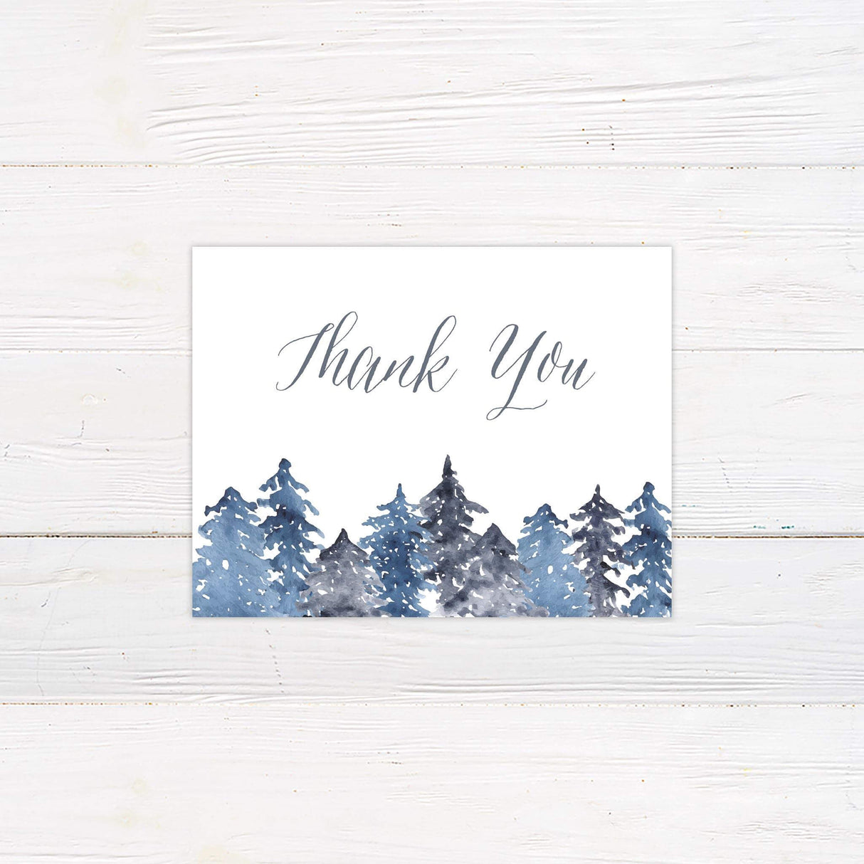 Thank you card with snowy watercolor pine trees in blue and gray tones and elegant calligraphy.