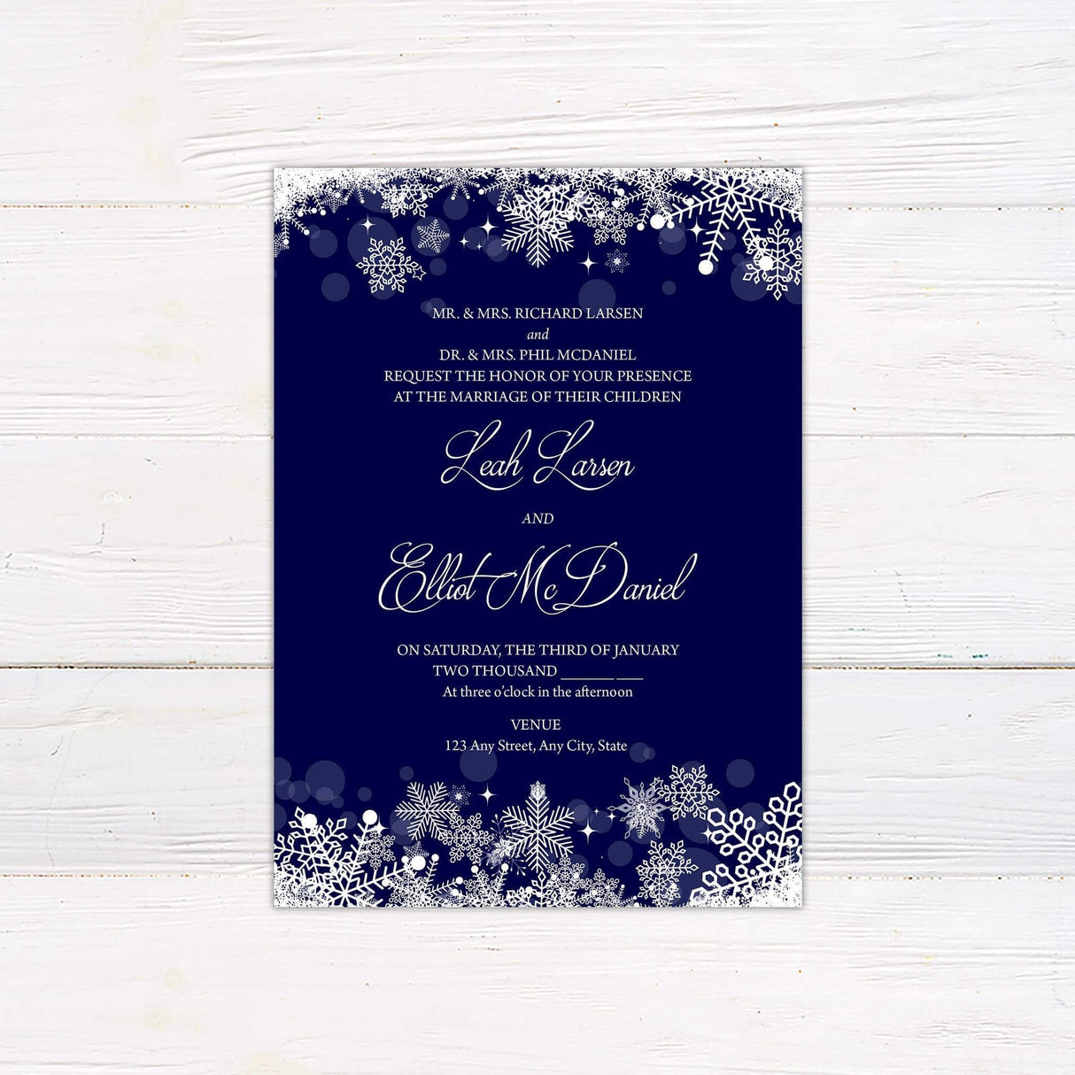 Navy blue wedding invitation with white snowflakes on top and bottom border and elegant script for a winter theme.