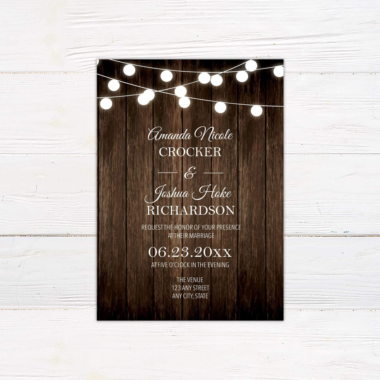 Rustic wedding invitation with wood background and glowing string lights, featuring script and serif fonts.
